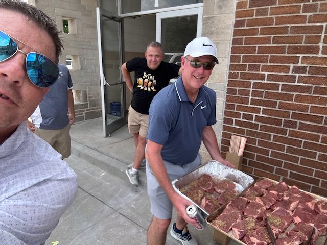 Members carrying trays of steaks to the grill