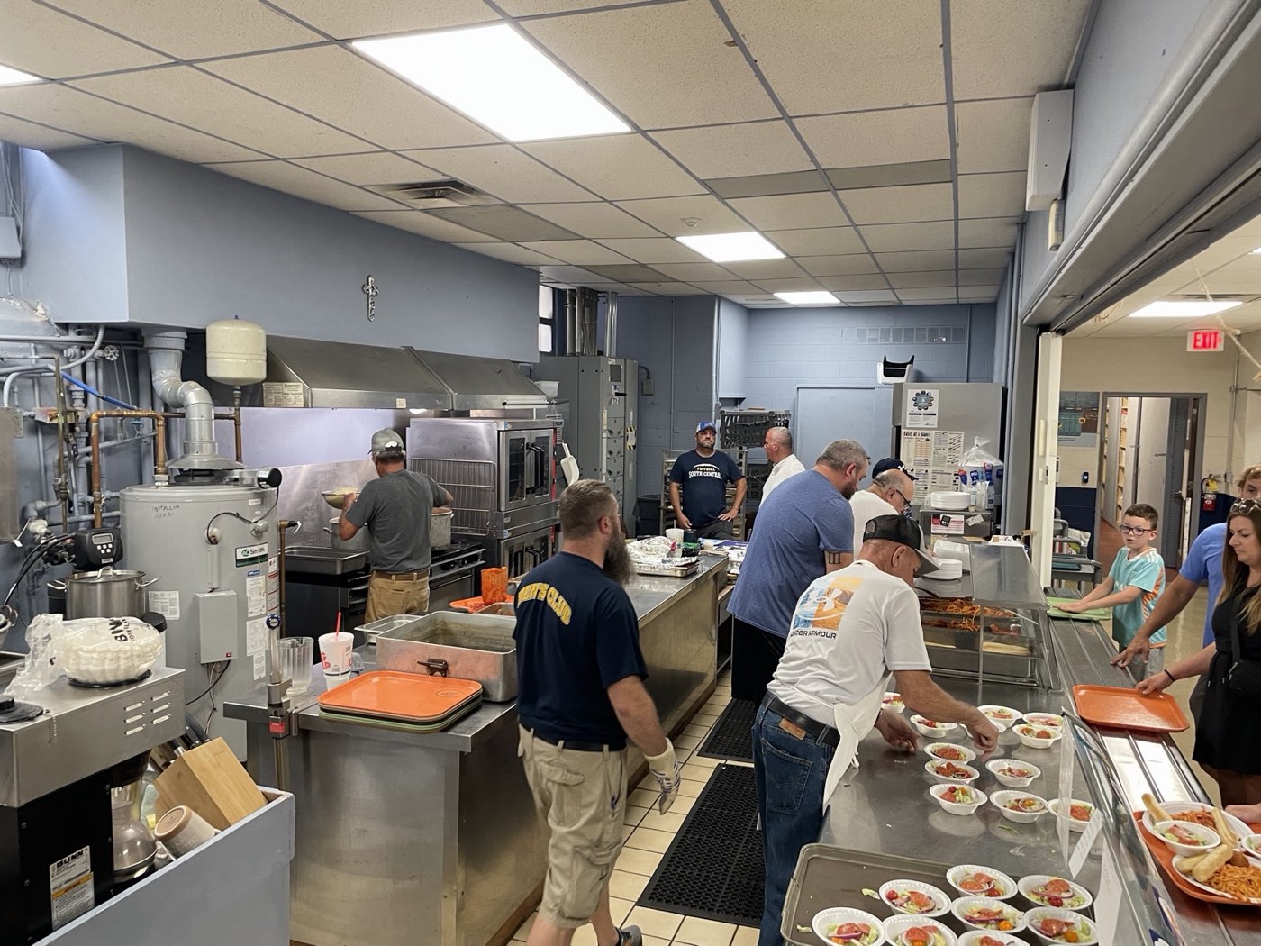 Volunteers filling salad bowls and plates along the cafeteria serving counter