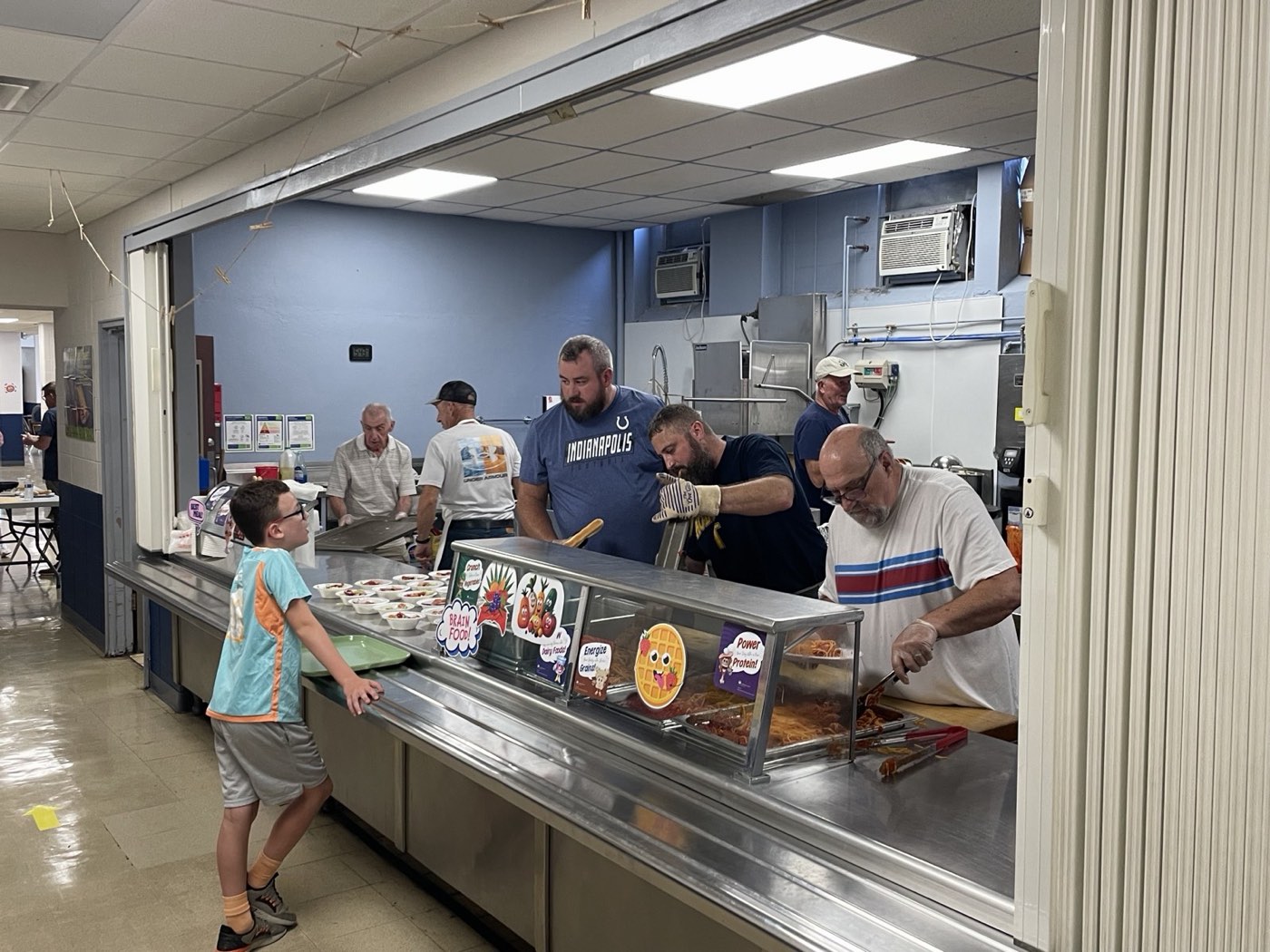 A guest sliding a tray along the counter as volunteers serve spaghetti and bread